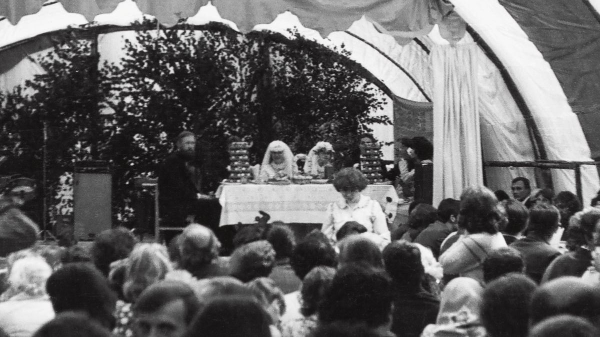 Il matrimonio dei Pudžiuvys. Gli sposi sono seduti a un tavolo che si trova su un palco sotto un tendone. Ci sono anche la cugina di Virgilijus e suo marito, perché si sono sposati lo stesso giorno.