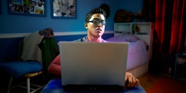 Ragazzo solo e al buio nella sua stanza che guarda immagini provocanti al computer