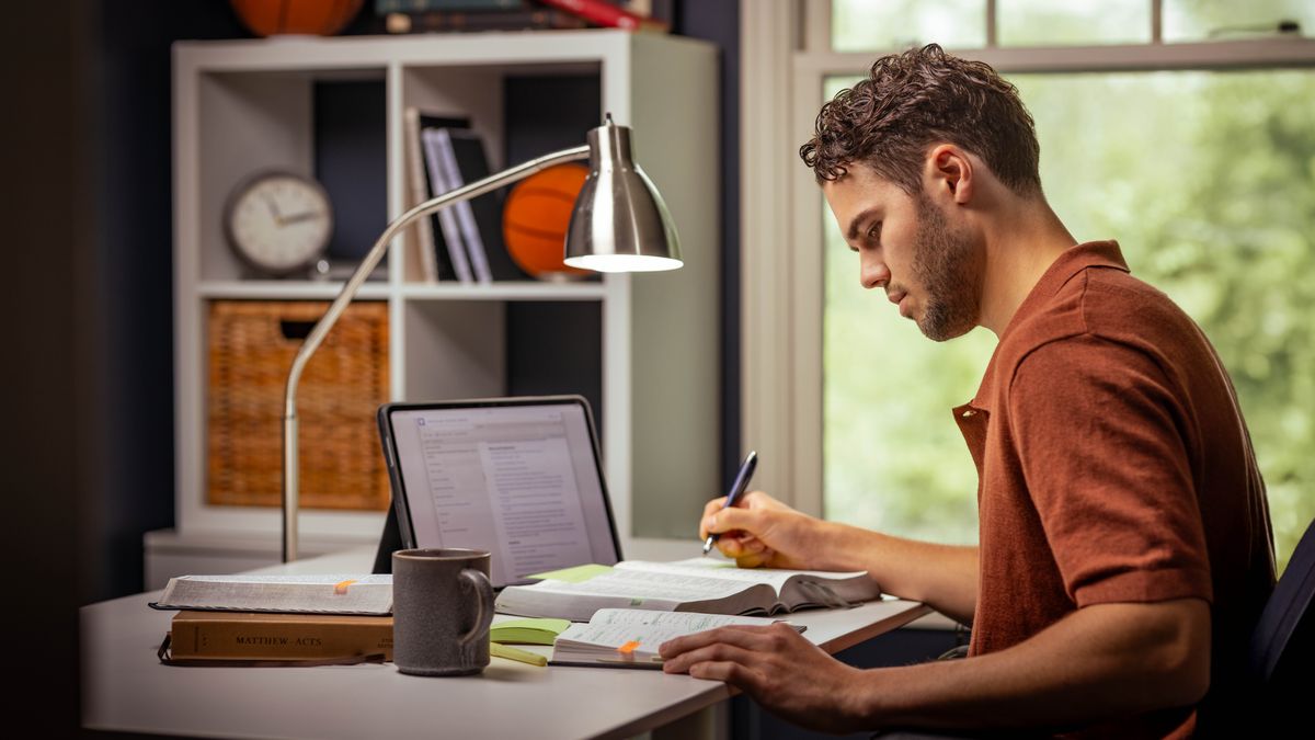 Un giovane fratello sta facendo il suo studio personale usando la Bibbia, un tablet e un taccuino. Scrive una nota nella Bibbia, che è aperta sul tavolo.