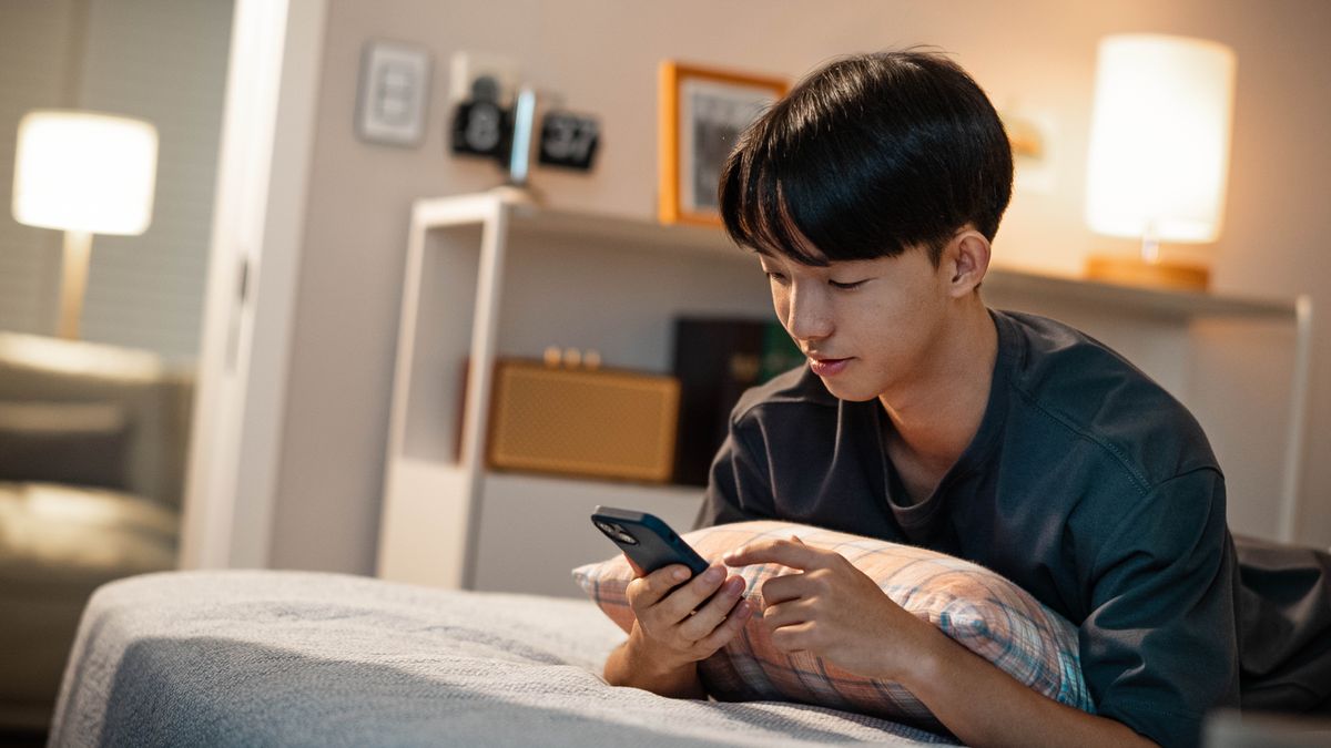 Un giovane fratello sdraiato sul letto guarda il cellulare.