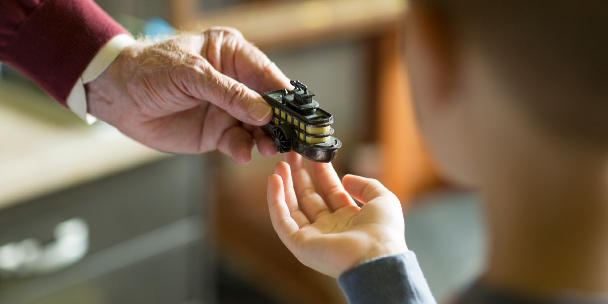 Un bambino che riceve in dono un temperamatite a forma di barca dalla mano di un anziano