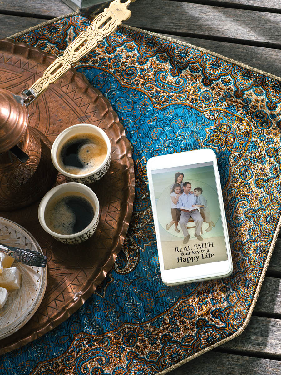 Uno smartphone accanto a due tazze di caffè. Sullo smartphone si vede la copertina dell’opuscolo “La vera fede, il segreto per una vita felice”.