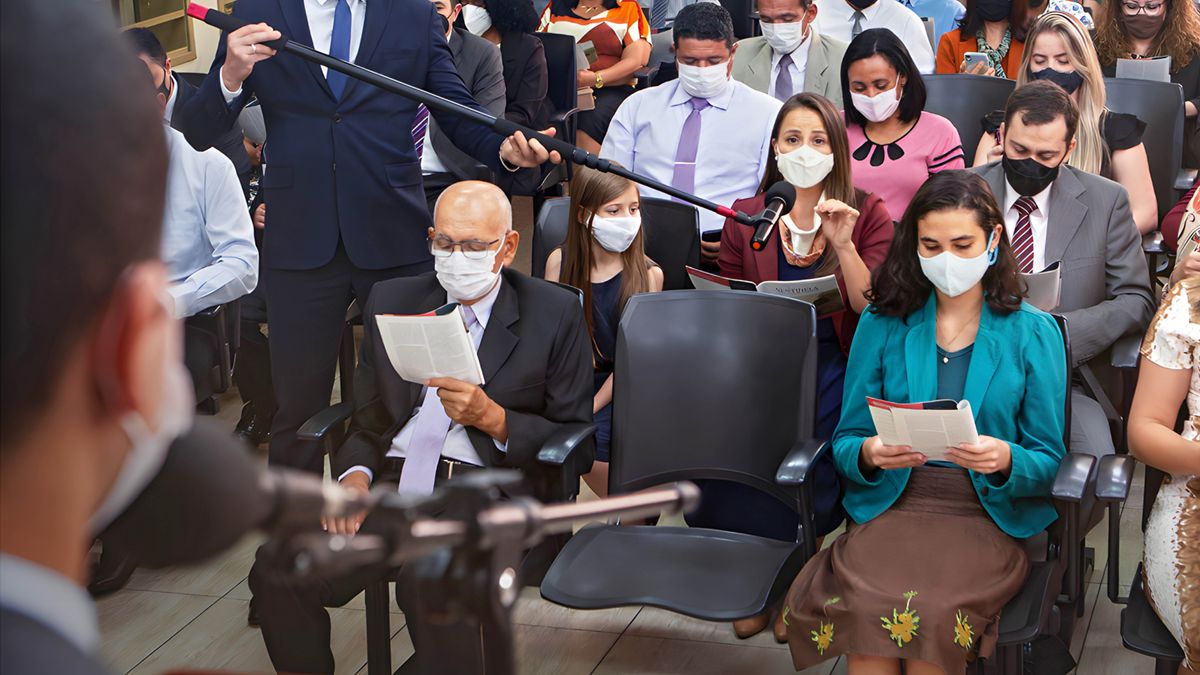Sedulur wédok njawab ing pertemuan ibadah. Ana sedulur lanang sing ngédarké mikrofon. Kabèh nganggo masker.