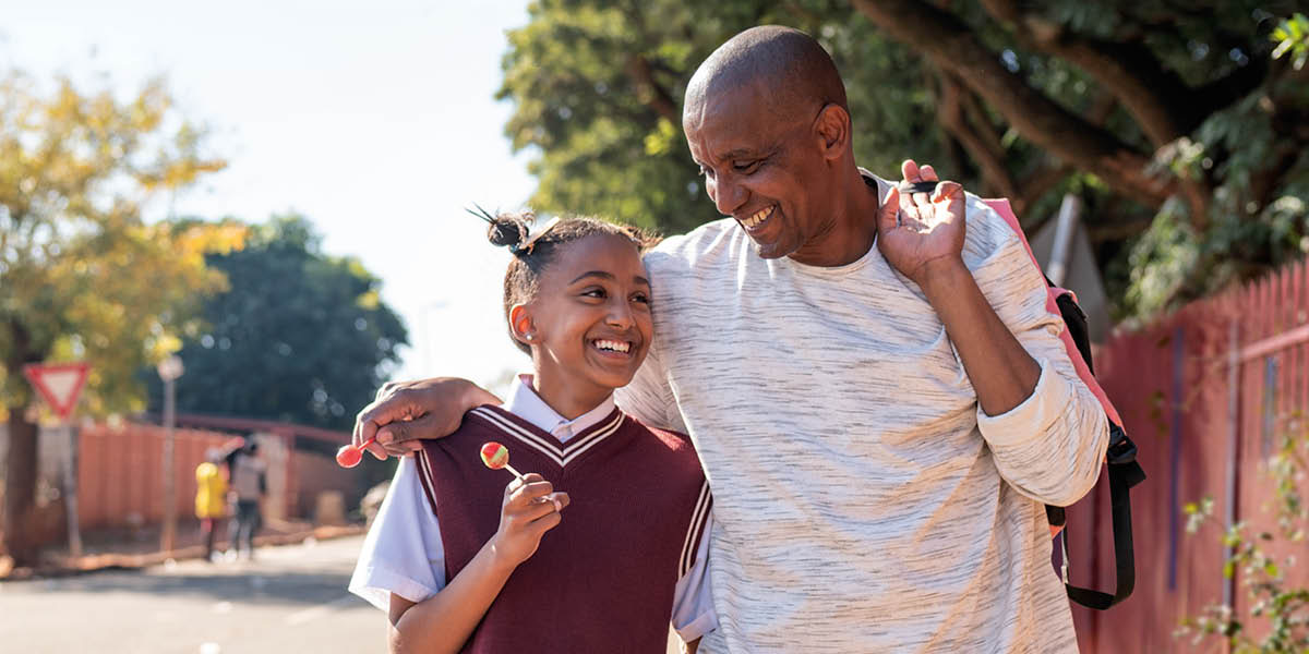 მამა თინეიჯერ ქალიშვილთან ერთად მომღიმარი სახით მიაბიჯებს ქუჩაზე.