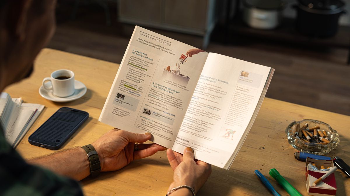 Еден човек ја чита лекција 40 од книгата „Радувај му се на животот засекогаш“. На масата има кутија со цигари и пепелник полн со отпушоци од цигари.