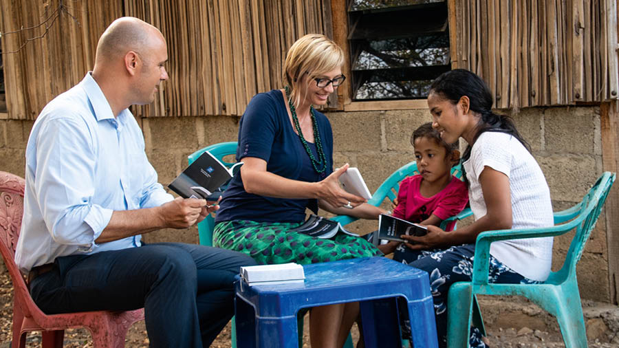 Vanessa and Alex conducting a Bible study outdoors with a mother and her child.