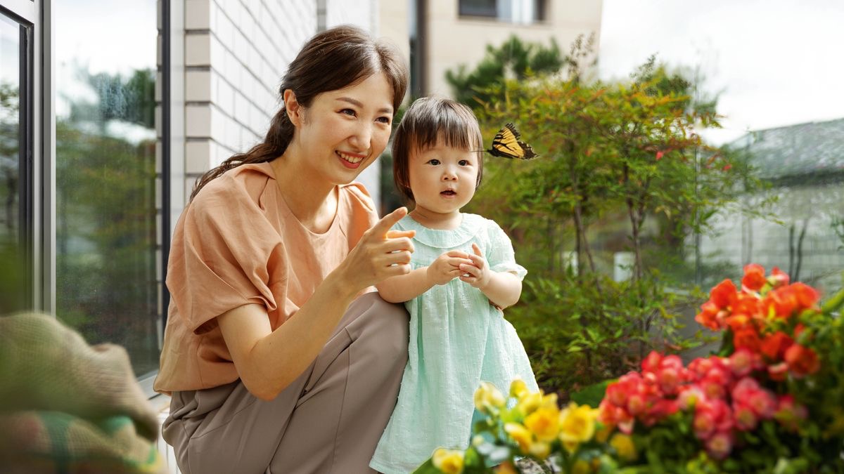 A mother pointing out a butterfly to her young daughter outside their apartment building in a city.