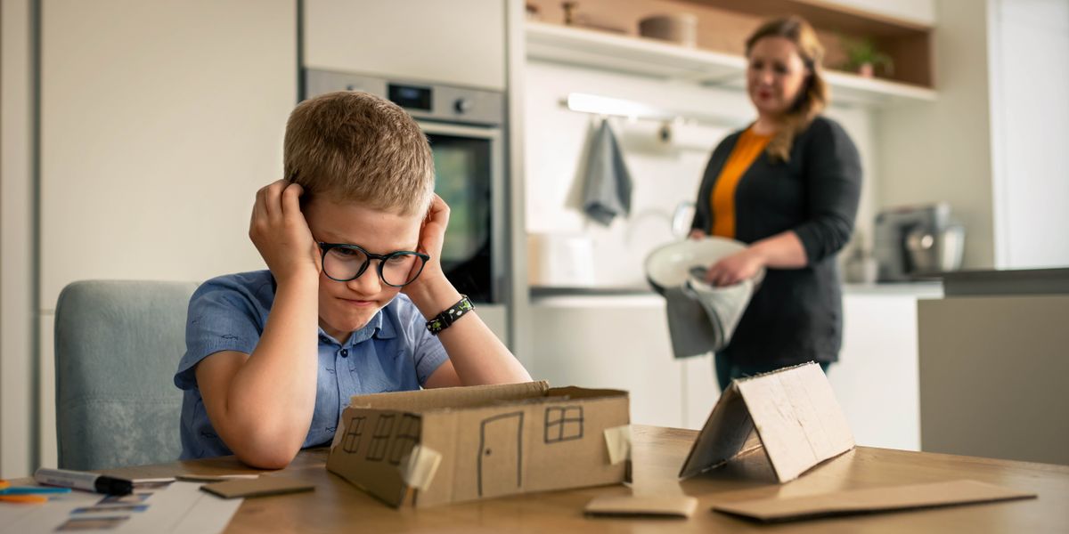 Wanfala smol boy hem frustrate bikos hem stragol for buildim wanfala smol cardboard haos. Mami blo hem no kwiktaem helpem hem bat standap lelebet farawe and observim hem.