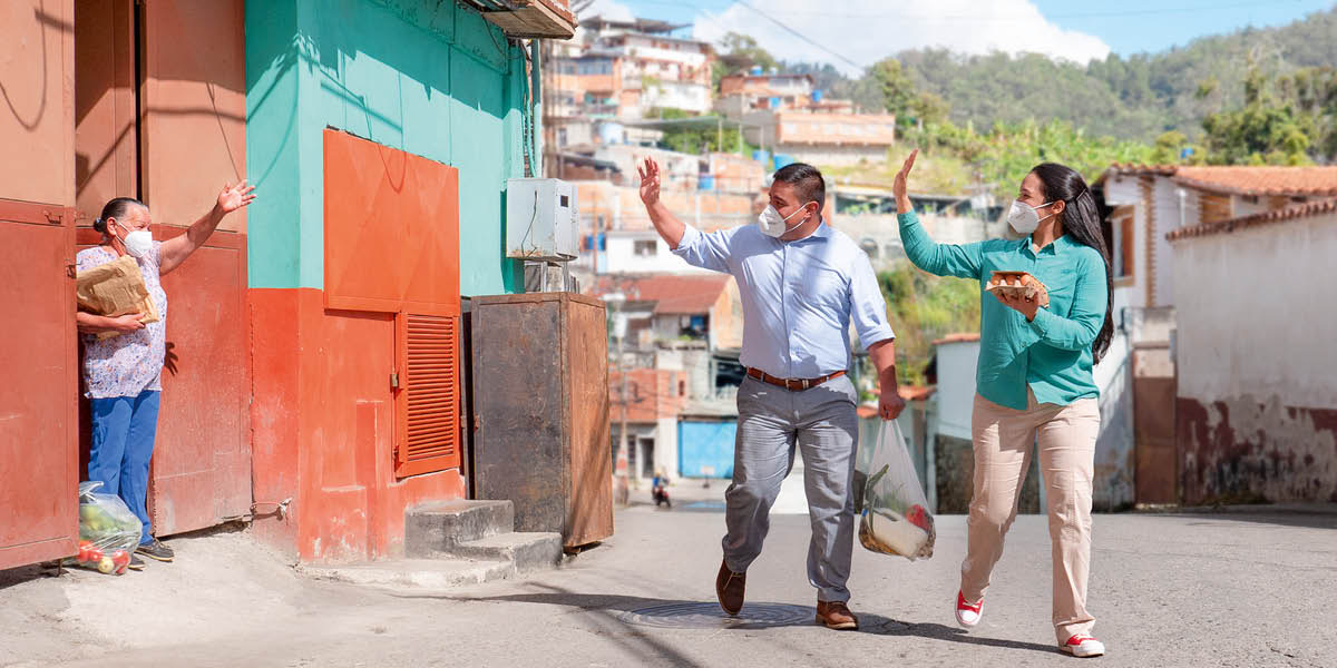 Um casal usando máscaras, entregando alimentos para uma irmã idosa.