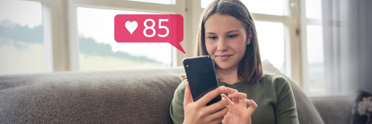 Uma jovem sorrindo e olhando para o celular. Ela recebeu 85 curtidas na rede social.