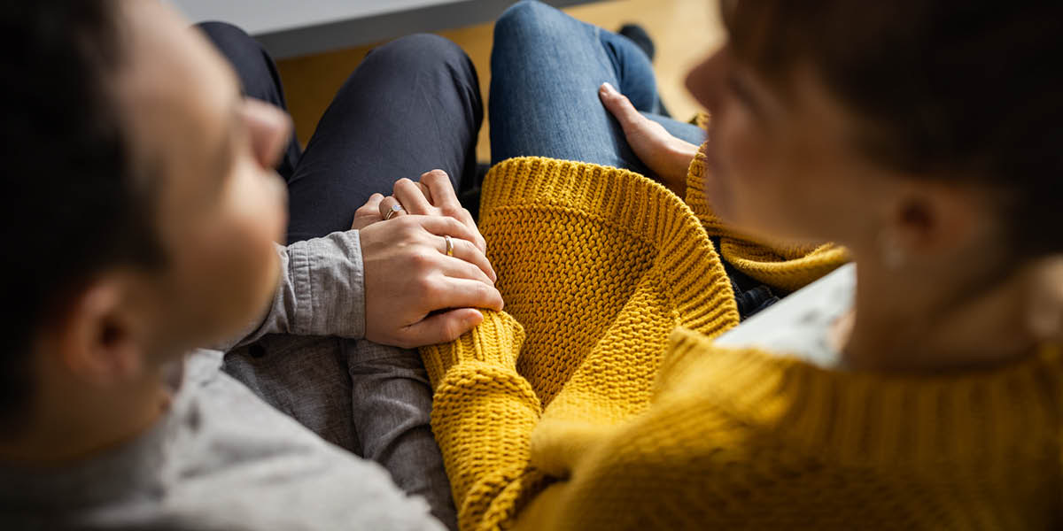 Un esposo y una esposa están sentados juntos y se toman de la mano mientras hablan.