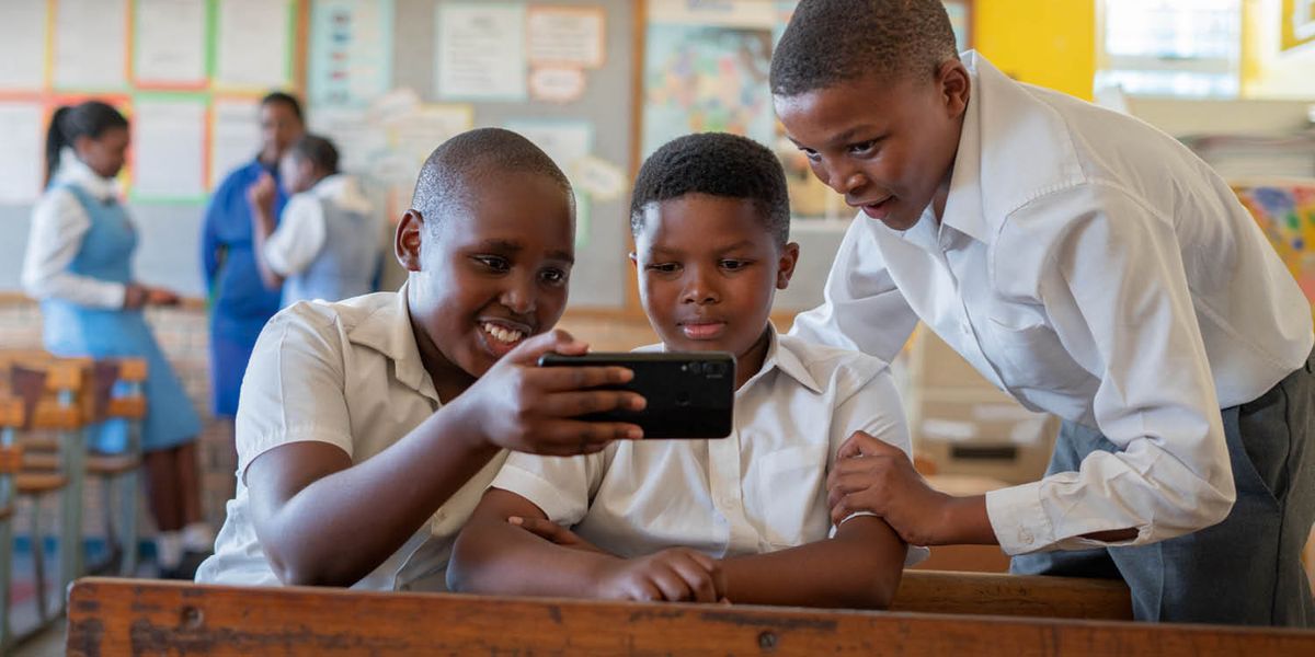 Tres niños mirando muy concentrados la pantalla de un teléfono.