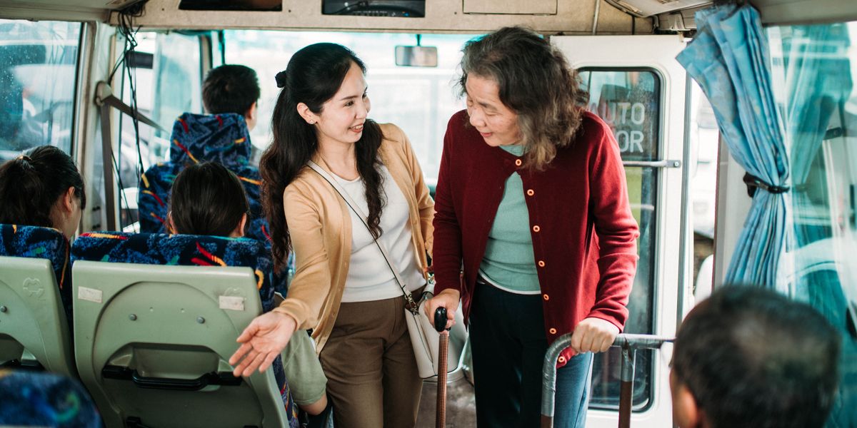 En un autobús, una joven amable ayuda a una señora mayor a sentarse.