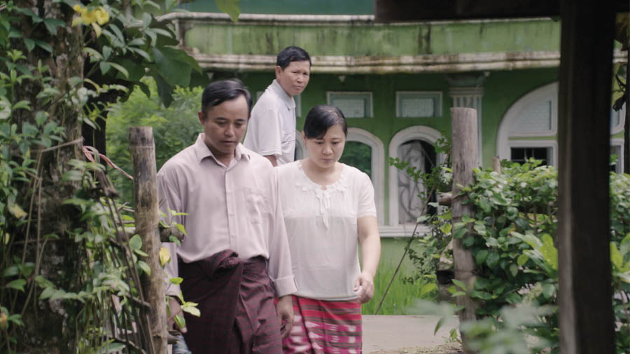 Una imagen del video Mostremos en la congregación el amor que nunca falla: A las viudas y a los huérfanos. Un vecino observa a dos Testigos que van a visitar a la hermana Myint y sus hijas.