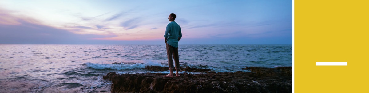 Lección 7. Un hombre de pie en unas rocas junto al mar mirando al horizonte después de la puesta del sol.