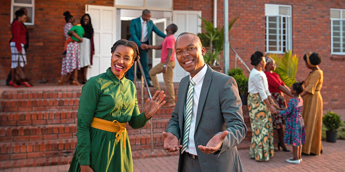 Umugabo n’umugore bariko baraha ikaze abashitsi babigiranye igishika ku Ngoro y’Ubwami.