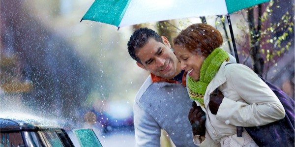 A husband holds an umbrella over his wife as he helps her into a car
