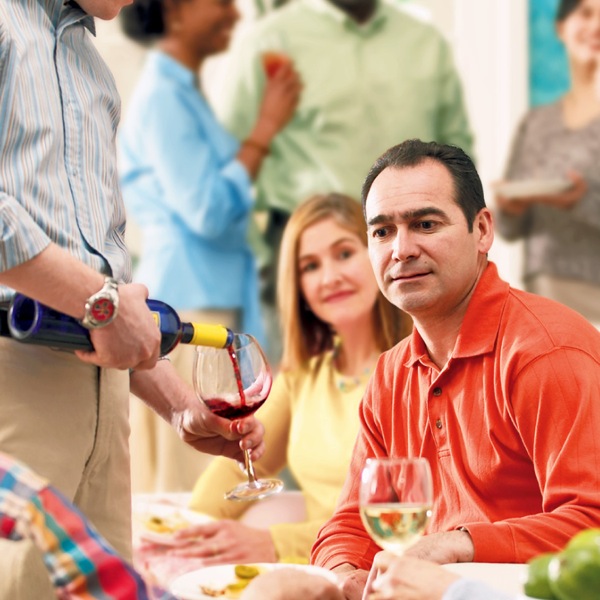 A man deciding whether or not he will drink a glass of wine at a gathering