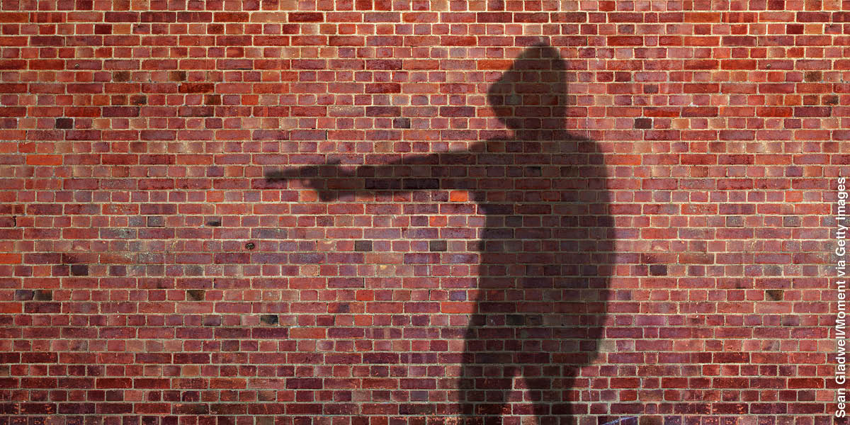A shadow on a brick wall of a person pointing a gun.