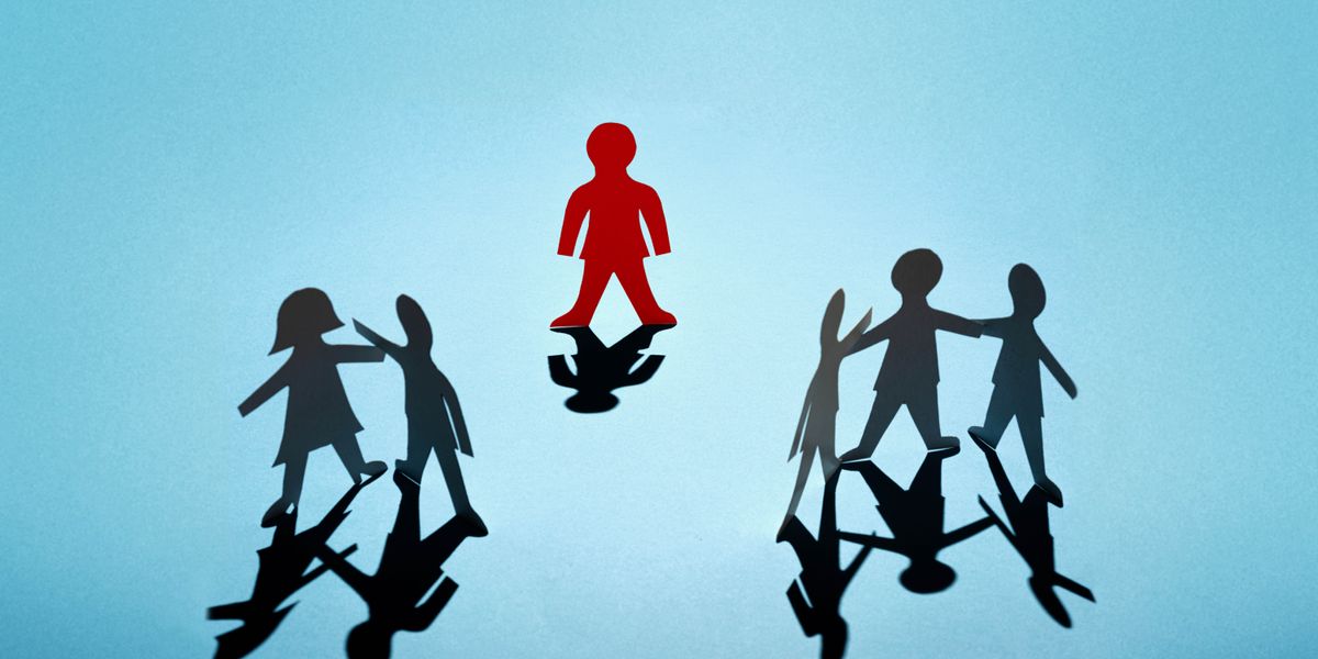 A paper doll standing alone, away from other paper dolls standing together.
