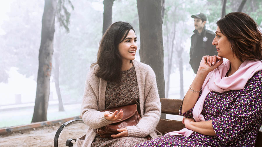 A sister witnessing to a woman on a park bench in a country where our work is banned as a police officer walks nearby.