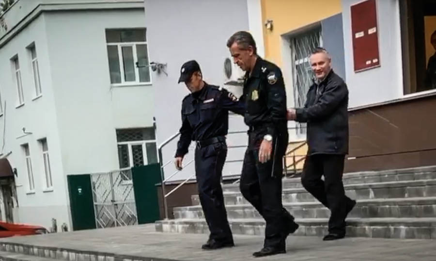 A scene from the video ‘Interview With Brother Dmitriy Mikhaylov.’ Dmitriy is led in handcuffs by two officers.