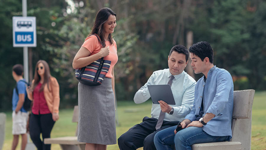 A couple using the “Enjoy Life Forever!” brochure to talk with a man at a bus stop.