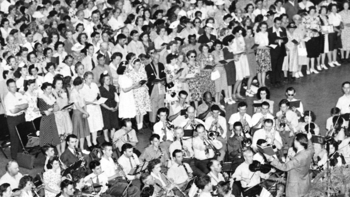 A scene from the video “Our History in Motion​—The Gift of Song, Part 2.” Brothers and sisters sing at a convention, accompanied by a live orchestra.