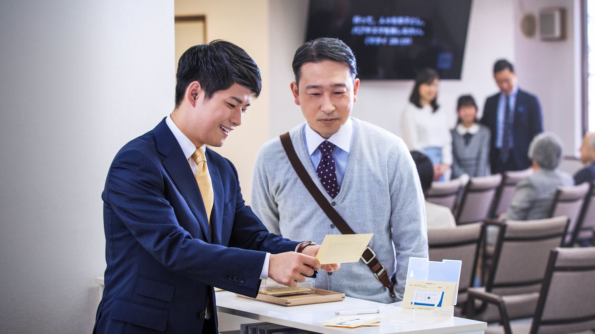 A younger elder conducting the “Watchtower” Study while an older brother, who is the reader, smiles at him.