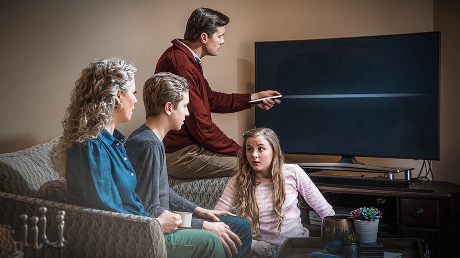 A Witness father turns off the television as his family sits nearby