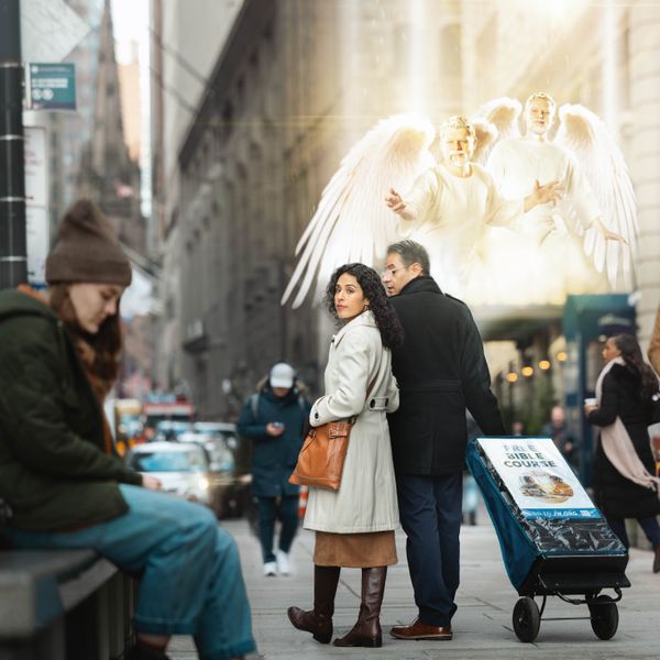 A couple walking with a public witnessing cart on a city street. Angels hover above and direct the sister to notice a distressed young woman sitting on a bench.