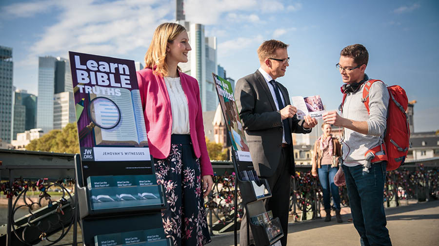 Jehovah’s Witnesses standing next to literature carts, talking to a man.