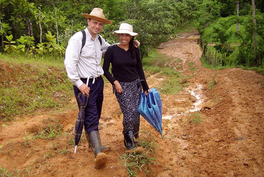 Donald och hans fru Nuria står på en lerig väg. De har hattar, ryggsäckar, paraplyer och gummistövlar.