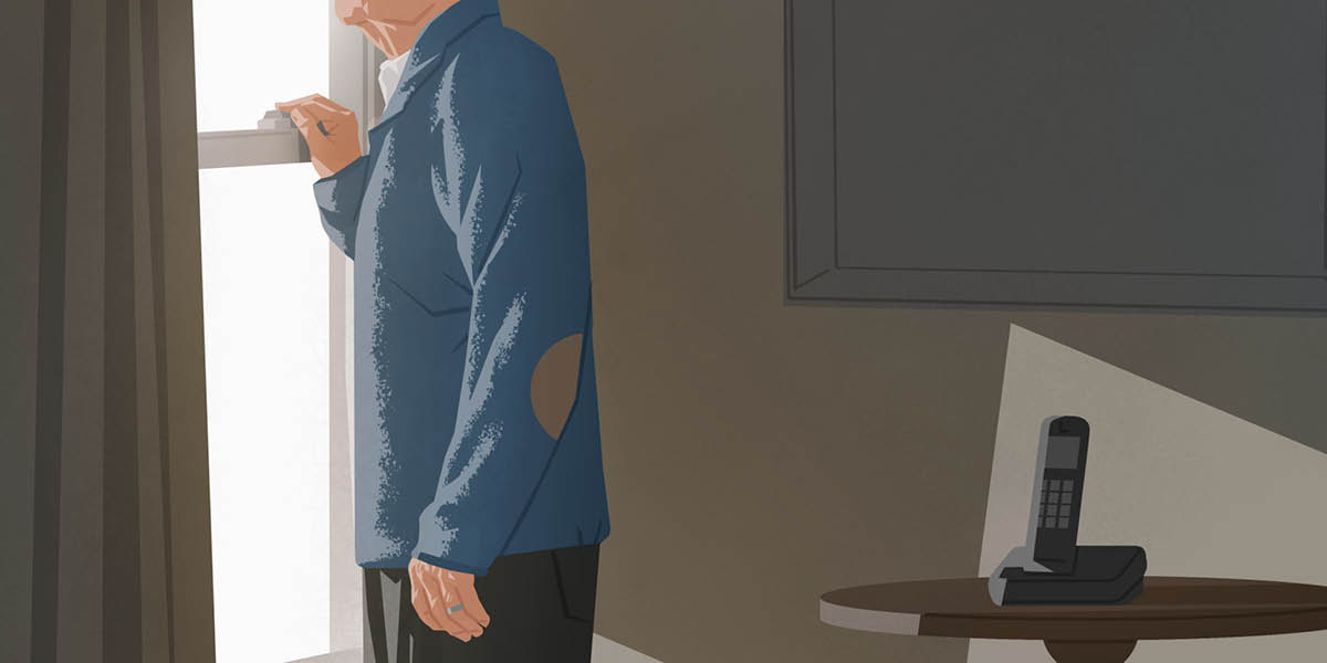 En äldre man tittar ut genom fönstret. På bordet bredvid står telefonen.