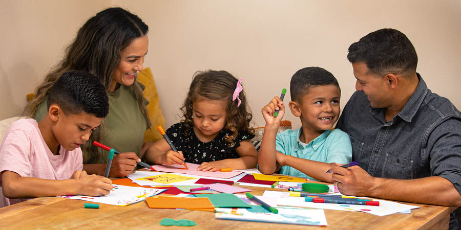 En mamma och en pappa hjälper sina barn att göra tackkort.