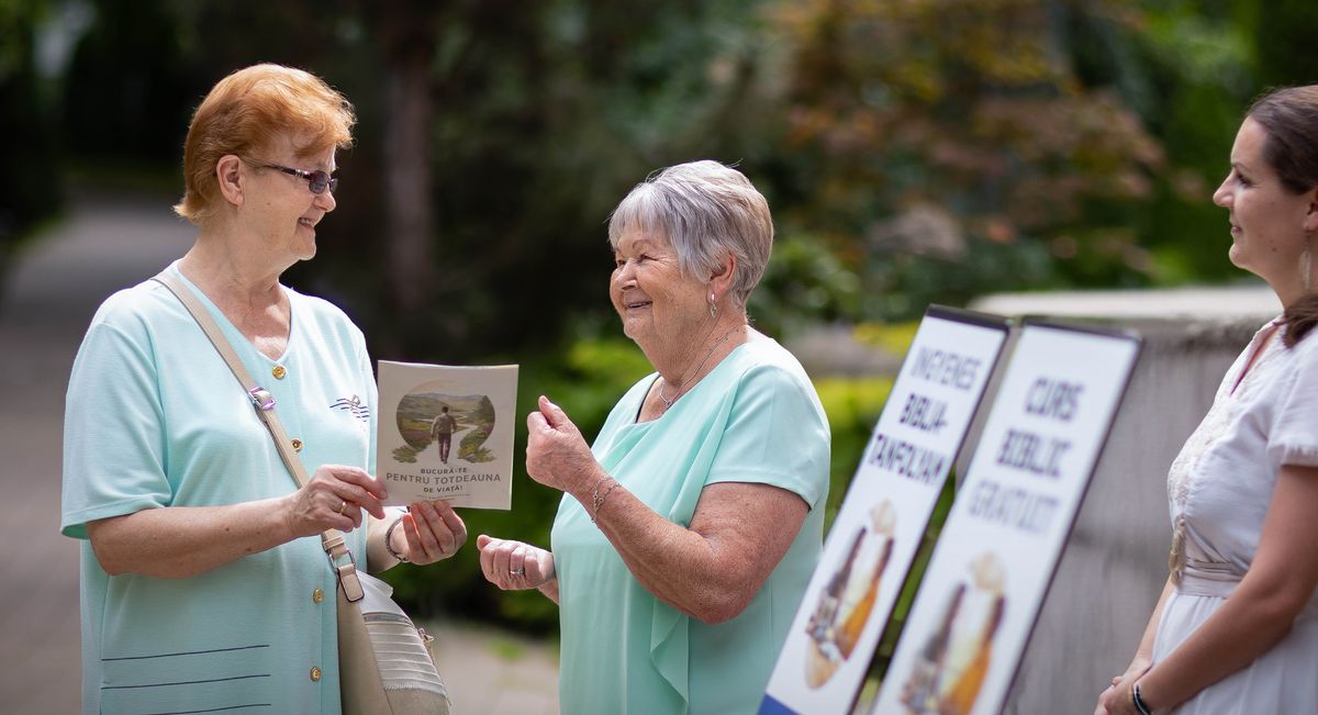 Ibolya och en annan syster står vid en litteraturvagn. Ibolya vittnar för en kvinna med hjälp av broschyren ”Ett hopp om en ljus framtid”.