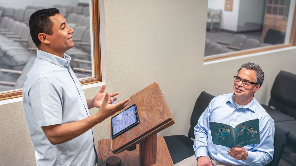 En äldste lyssnar när en broder övar ett tal. Äldstebrodern har broschyren ”Bli bättre på att högläsa och undervisa” uppslagen.