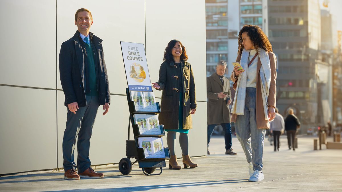 Ett par vid en litteraturvagn och en kvinna som går förbi tittar på skylten ”Gratis bibelkurs”.