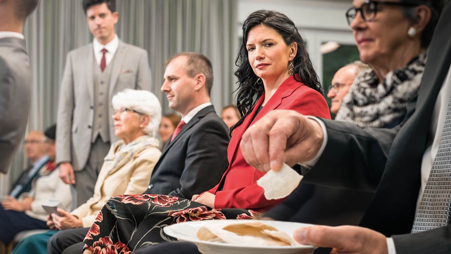 En syster tittar uppmärksamt på en broder som äter av brödet på minneshögtiden.