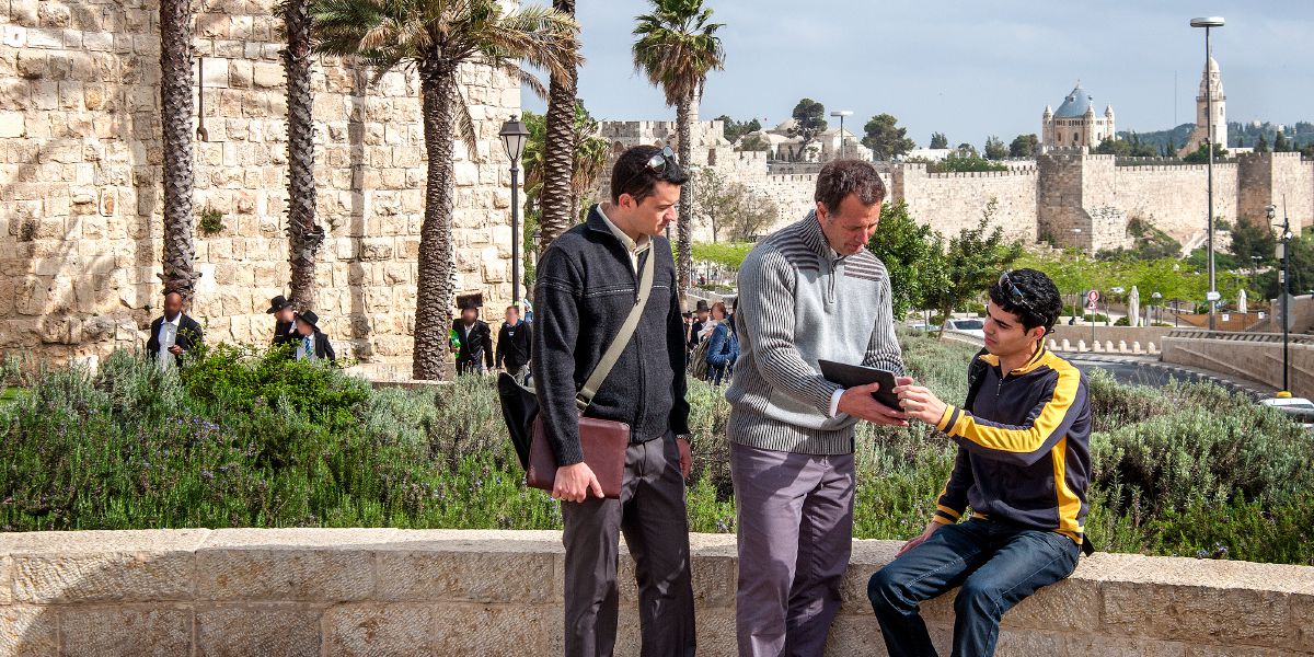 Två Jehovas vittnen i Israel använder en surfplatta för att predika för en man
