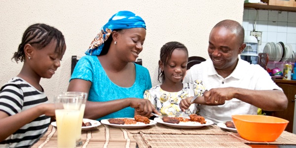 Mume na mke wenye furaha wakila chakula pamoja na binti zao wawili