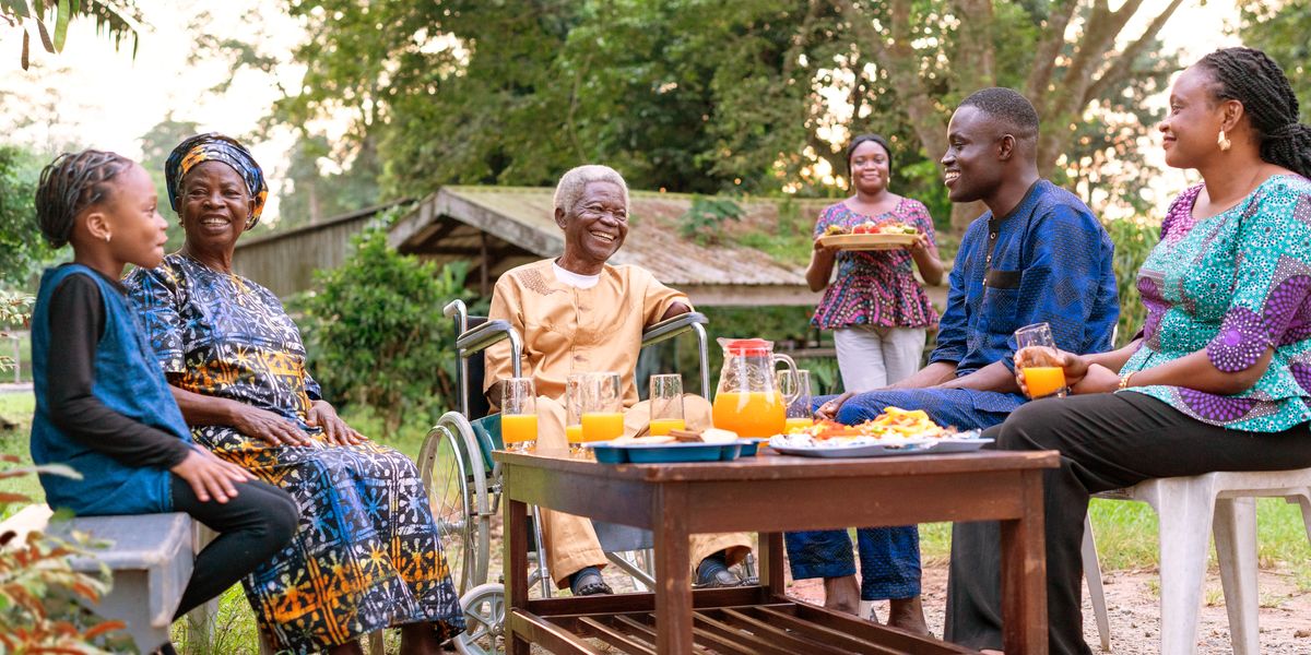 Mwanamume mwenye umri mkubwa aliyepoteza mikono yake vitani, ameketi nje kwenye kiti cha magurudumu akifurahia mlo pamoja na familia yake.