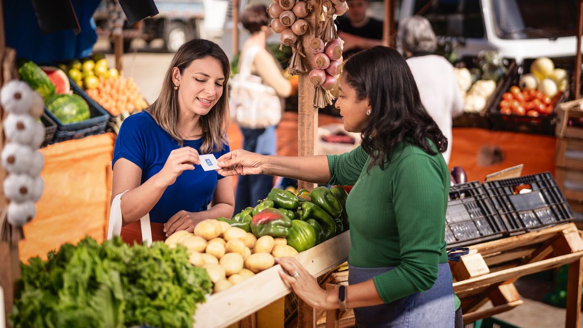 พี่​น้อง​หญิง​กำลัง​ให้​นาม​บัตร jw.org กับ​แม่​ค้า​ที่​ตลาด