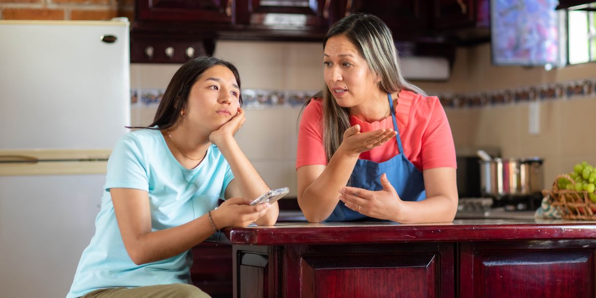 Isang teenager na babae na may hawak na phone at nalulungkot habang pinapayuhan ng nanay niya.