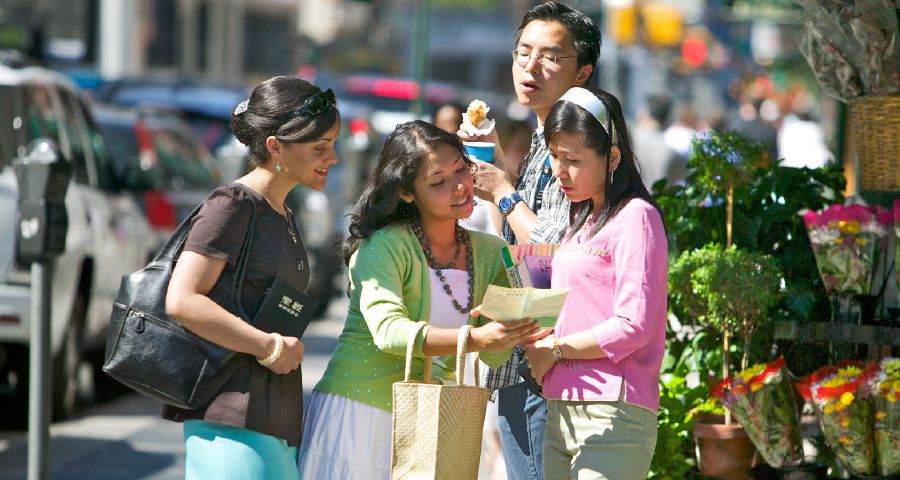 Dos hermanas predicándole a una muchacha en la calle y un joven asomándose por encima de ellas para averiguar de qué están hablando.