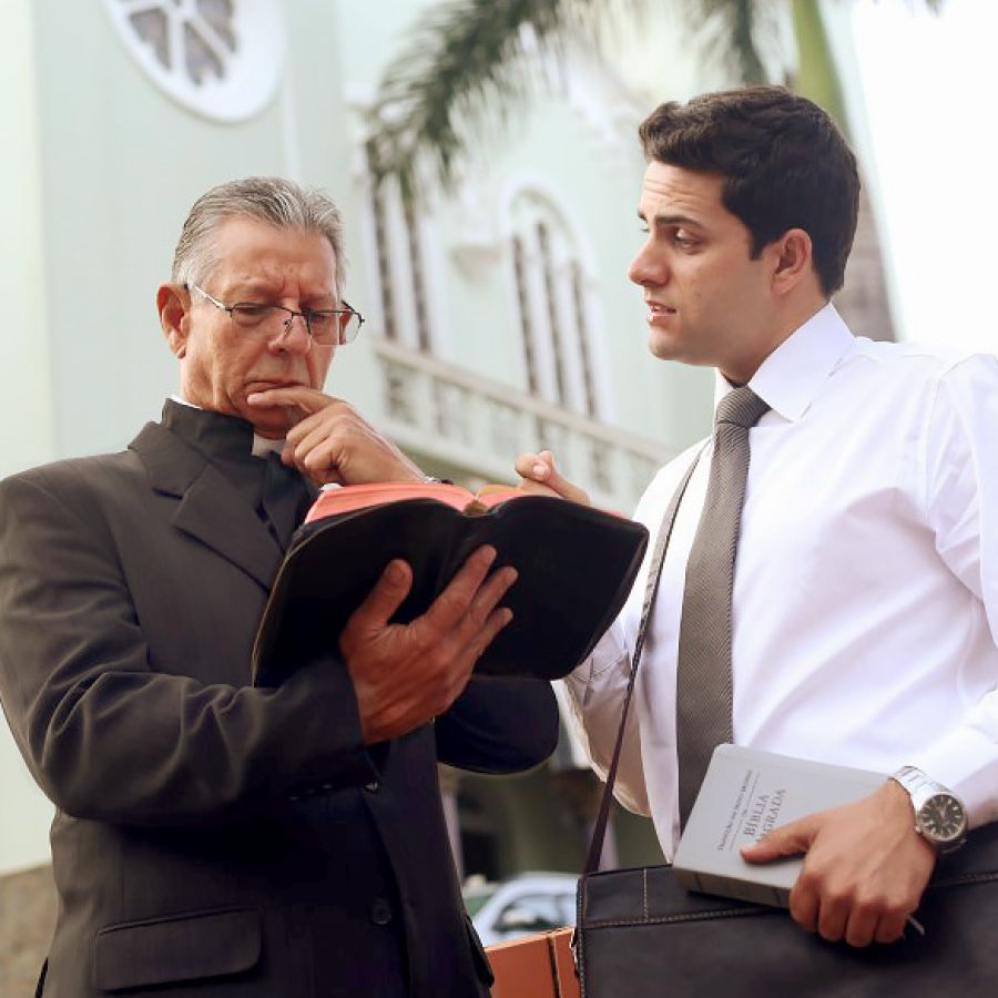 Un sacerdote católico leyendo con atención un texto en su Biblia mientras un hermano le predica.