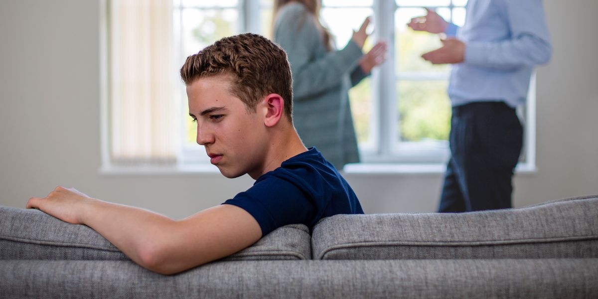 Сумний хлопець-підліток сидить на дивані; він відвернувся від батьків, які сваряться одне з одним.