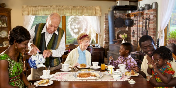 Люди різного віку і рас разом частуються; збоку через вікно заглядає злий лев