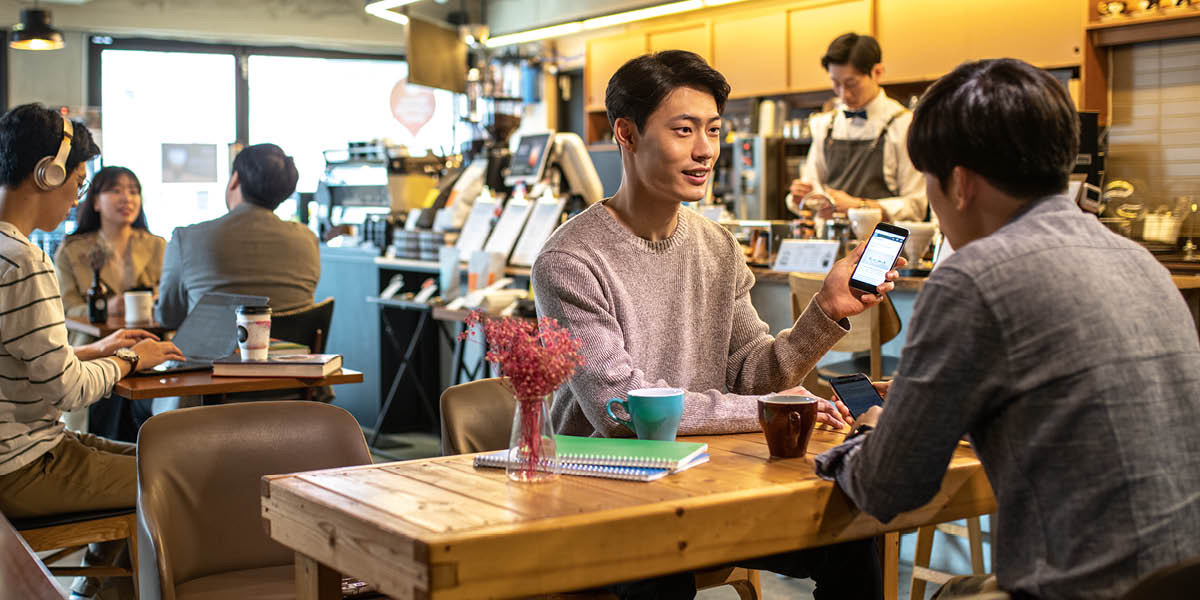 Чоловік за столиком у кафе показує другу екран свого смартфону.