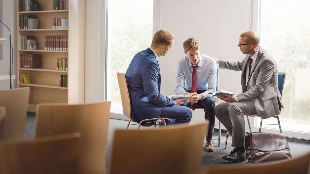 Hai trưởng lão nhân từ chia sẻ các câu Kinh Thánh với một anh trẻ. Một trưởng lão đặt tay lên vai của anh ấy trong khi nói chuyện.